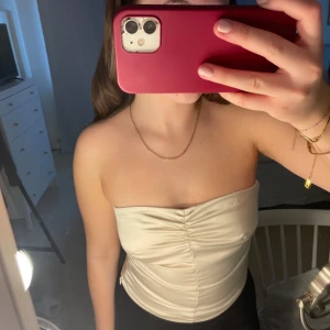 Beige tubtopp - Snygg beige tubtopp i satin med rynkdetalj framtill. Perfekt för en stilren look. Passar bra till både jeans och kjol. Toppen är från Bik bok i storlek S.