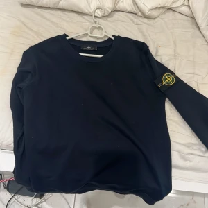 Mörkblå tröja från Stone Island - Säljer en snygg mörkblå tröja från Stone Island med det ikoniska märket på ärmen. Tröjan har en klassisk design med långa ärmar och rund hals. Perfekt för en stilren look.