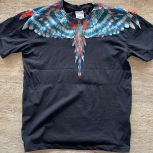 Marcelo Burlon T-shirt - Snygg svart t-shirt från Marcelo Burlon med ett iögonfallande färgglatt vingmönster över axlarna och bröstet. Perfekt för dig som vill sticka ut med en unik design. Tillverkad i mjuk bomull för extra komfort.