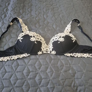 Intimissimi bh  - Elegant svart bh från Intimissimi med vackra spetsdetaljer i vitt. Den har justerbara axelband och en klassisk hakknäppning bak. Perfekt för att ge en lyxig känsla till din outfit. Tyvärr den är utan storlekslapp. 