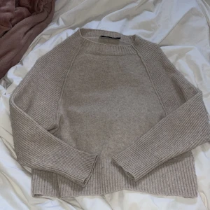 Beige stickad tröja från Oui - Säljer en stilren beige stickad tröja från Oui. Tröjan har långa ärmar och en ribbad design som ger en klassisk look. Perfekt för kyligare dagar och enkel att matcha med olika outfits.