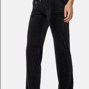 Svarta juicy byxor  - Snygga svarta mjukisbyxor med snörning i midjan och praktiska fickor både fram och bak. Byxorna har en avslappnad passform och är perfekta för en bekväm stil. Dekorativa knappar på bakfickorna ger en extra touch.