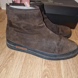 Bruna mockaboots från GANT - Snygga bruna boots i mocka från GANT.  De har en stilren design med dragkedja baktill för enkel på- och avtagning. Insidan är fodrad för extra komfort och värme. Perfekta för kyligare dagar. Sparsamt använda.