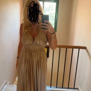 Champagnefärgad balklänning - Elegant champagnefärgad långklänning med djup v-ringning och öppen i ryggen. Köptes från bubbelroom för 1599kr. Lite smutsig längst ner men går bort i tvätten på nolltid! 