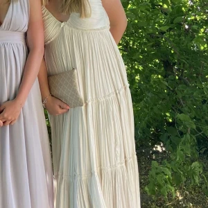 Långklänning i ljusa toner - Två eleganta långklänningar i ljusa toner. Den ena är vit och den andra ljuslila, båda med djup v-ringning och plisserade detaljer. Perfekta för sommarens festligheter.