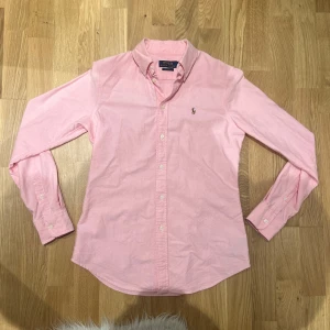 Rosa skjorta från Polo Ralph Lauren - Snygg rosa skjorta från Polo Ralph Lauren i bomull. Perfekt för en stilren look med den klassiska broderade loggan på bröstet eller en varm sommardag. Fint skick på skjortan enbart lite skrynklig nu. Storlek S. Hör gärna av dig vid frågor eller funderingar. Priset går att slipa på vid snabb affär. 