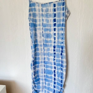 Blå och vit klänning med batikmönster - Snygg ärmlös klänning i blått och vitt med ett coolt batikmönster. Perfekt för sommardagar med sin lätta och luftiga design. Klänningen har en åtsittande passform och är gjord i ett mjukt material som känns skönt mot huden.