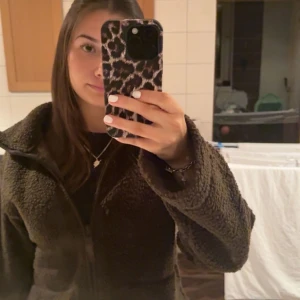 Grön teddyjacka med dragkedja - Mysig grön teddyjacka med dragkedja framtill. Perfekt för kyliga dagar med sin mjuka och fluffiga textur. Jackan har en hög krage och långa ärmar för extra värme.