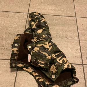 Camouflage regnjacka från Urban Pup till hund  - Snygg camouflage regnjacka från Urban Pup med texten 'RAIN STORM' längs dragkedjorna. Perfekt för att hålla sig torr och stilren i regnigt väder. Jackan har en cool design med gröna och beige toner. Till hund 