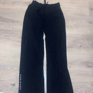 Svarta byxor från Röhnisch - Snygga svarta byxor från Röhnisch med snörning i midjan. Perfekta för en avslappnad stil. Byxorna har en rak passform och är tillverkade i ett mjukt material för extra komfort. Med ett tryck ”röhnish” på benet