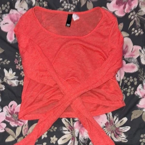 Korallfärgad topp - Säljer en snygg korallfärgad topp. Toppen har en rund halsringning och är långtärmad. Den är väldigt tunn så linne behövs under då den e inprincip genomskinlig. Den är gjord i ett mjukt och bekvämt material.
