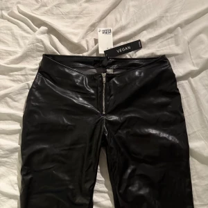 Viral lågmidjade skin byxor  med dragkedja - Snygga svarta lågmidjade skinnbyxor från h&m med en framträdande dragkedja framtill. Byxorna har en tight passform och är tillverkade i ett syntetmaterial som ger en glansig look. Perfekta för en trendig stil. 