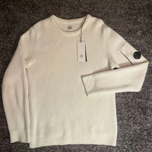 Vit stickad tröja från C.P. Company - Säljer en stilren vit stickad tröja från C.P. Company. Tröjan har långa ärmar och en rund halsringning.                                          Nypris ligger på 2600