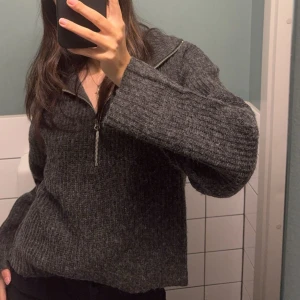 Mörkgrå stickad tröja med dragkedja - Säljer en mysig mörkgrå stickad tröja med dragkedja vid halsen. Perfekt för kyliga dagar och enkel att matcha med olika outfits. Tröjan har långa ärmar och en avslappnad passform.