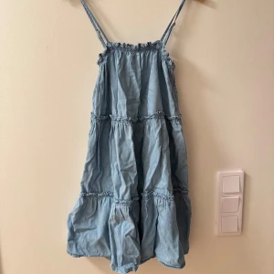 Ljusblå klänning från Primark - Säljer en söt ljusblå klänning från Primark med smala axelband och volangdetaljer i storlek 36. Klänningen har en avslappnad passform och är tillverkad i denimliknande material.