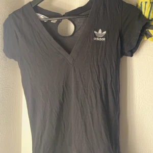 Svart v-ringad t-shirt från Adidas - Snygg svart t-shirt från Adidas med v-ringning och korta ärmar. Den har en liten Adidas-logga på bröstet och en stilren design. Perfekt för en avslappnad look.