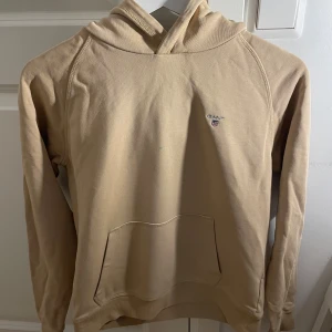 Beige hoodie från GANT - Säljer en stilren beige hoodie från GANT. Tröjan har en klassisk design och en liten logotyp på bröstet. Perfekt för en avslappnad look. Frågor skriv!