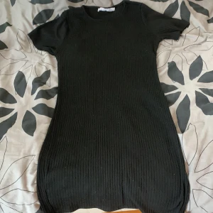 Svart ribbad klänning från 157 - Snygg svart ribbad klänning från 157 i storlek L. Tillverkad av 80% polyester och 20% viskos. Perfekt för en stilren look med korta ärmar och en bekväm passform.