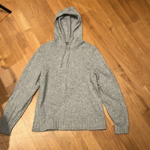 Grå stickad hoodie Dressmann - Säljer en mysig grå stickad hoodie med långa ärmar och ribbade muddar. Perfekt för kyliga dagar. Den har en justerbar huva med snören för extra komfort. För liten för mig som är 183. Sitter pytte lite löst vid midjan.