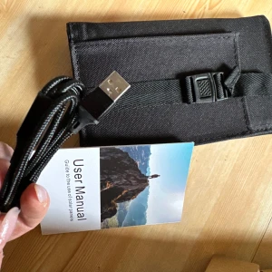 Svart solcellsladdare med USB-kabel - Praktisk svart solcellsladdare med tillhörande USB-kabel och karbinhake. Perfekt för att ladda dina enheter med solenergi när du är på språng. Kompakt design som enkelt kan fällas ihop och tas med överallt.