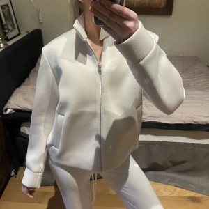 Beige jacka från COS - Säljer en stilren beige jacka från COS med dragkedja och hög krage. Jackan har en minimalistisk design med långa ärmar och två fickor framtill. Perfekt för en modern och enkel look.
