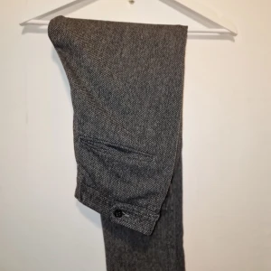 Grå kostymbyxor med knappar - Snygga grå kostymbyxor med ett diskret mönster. Byxorna har en klassisk passform med knappar vid midjan och bakfickor.