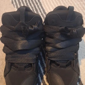 Svarta chunky sneakers med bred snörning - Svarta sneakers med riktigt breda snören och chunky sula. Skorna har rund tå, meshdetaljer på sidorna och är tillverkade i syntetmaterial. Perfekta för dig som gillar en streetstyle-look med extra attityd.