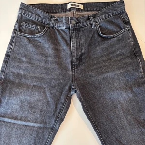 Svarta jeans från Woodbird, 32/32 - Säljer ett par svarta jeans från Woodbird i modellen Doc Grow Jeans. Dom är mer svart/mörkgrå än vad det ser ut som. Passformen är ganska relaxed med en vanlig gylf. Jeansen är använda enstaka gånger så otroligt bra skick. HÖR AV DIG VID MINSTA FUNDERING….