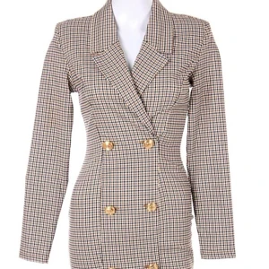 Rutig blazerklänning från Amisu - Snygg blazerklänning från Amisu i storlek 36 med rutigt mönster i beige, svart och brunt. Klänningen har dubbelknäppning med guldiga knappar, markerad midja och långa ärmar. Perfekt för dig som gillar en chic och trendig look.