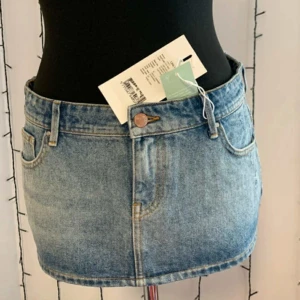 Blå jeanskjol från ONLY - Supersnygg ljusblå jeanskjol från ONLY med klassisk femficksdesign och bälteshällor. Kjolen är kort och har en rak passform som ger en fräsch och trendig look. Perfekt att matcha med en crop top eller hoodie för en chill vibe.