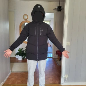 Svart dunjacka från Sail Racing - Säljer en svart dunjacka från Sail Racing med huva och två bröstfickor med dragkedja. Jackan är lång, har en clean look och är perfekt för kalla dagar. Materialet är syntet och dun, och jackan har en normal passform med långa ärmar. Passar personer mellan 165-175. Bara använd i 1 vinter.