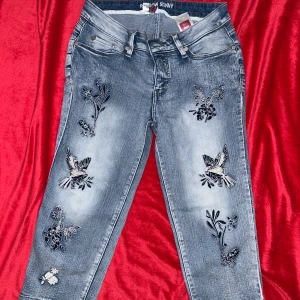 Blå skinny jeans med broderi - Snygga blå skinny jeans från Rainbow med broderade fåglar och blommor på framsidan. Jeansen har klassisk femficksdesign, normal midja och croppad längd. Perfekta för dig som vill ha ett par jeans med coola detaljer och unik stil.