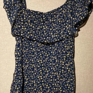 Blommig blå kortklänning från ICHI - Supersöt blå kortklänning från ICHI i storlek XS med ljust blommigt mönster. Klänningen har volangdetaljer vid axlarna och en mjuk, flowy passform. Perfekt för dig som gillar romantisk stil och vill ha något som sticker ut lite extra.