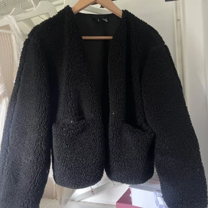 Svart teddyjacka med fickor - Mysig svart teddyjacka från hm med två stora fickor framtill.  Utan dragkedja, man knäpper denna. Perfekt inför hösten.