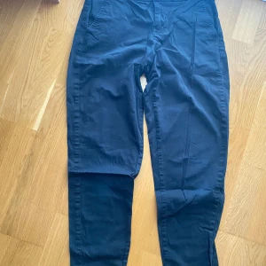 Mörkblå chinos med raka ben - Snygga mörkblå chinos med raka ben och klassiska fickor både fram och bak. Byxorna har bälteshällor och stängs med knappar framtill. Perfekta för en clean och stilren look, passar till både skjorta och t-shirt.