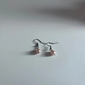 Rosa pärlörhängen med krok - Snygga örhängen med ljusrosa pärlor som hänger i enkla krokar av metall. Perfekta för dig som gillar en söt och stilren look. Pärlorna har en fin glans och ger ett elegant intryck.