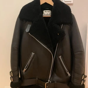 Svart pälsjacka Acne Studios - Nypris är 29 000kr. Riktigt fet svart pälsjacka från Acne Studios med bred krage, bälte i midjan och coola dragkedjor. Jackan är gjord i äkta lammull och skinn, har stora fickor och snygga spännen vid ärmsluten. Perfekt för dig som vill sticka ut med en lyxig och tidlös look.