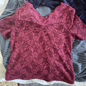 Vinröd spetsblus med blommönster - Vinröd blus i spets med blommigt mönster och v-ringad hals. Korta ärmar och genombrutet tyg ger en romantisk vibe. Perfekt för dig som gillar detaljer och vill sticka ut lite extra.skriv vid intresse. SPARSAMT ANVÄND 
