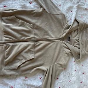 Beige hoodie med dragkedja Gina Tricot - Säljer en beige hoodie från Gina Tricot i storlek XS. Tröjan har huva, långa ärmar, två stora fickor framtill och dragkedja hela vägen. Materialet är mjukt och känns skönt mot huden, perfekt för chill dagar. Enkel och stilren design som är lätt att matcha.