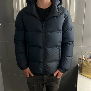 Colmar Dunjacka Mörkblå  - Nu säljer vi denna mörkblåa dunjacka från Colmar med huva och dragkedja framtill. Storlek 46, skick 9/10. Jackan är quiltad och har en clean, puffig look med logga på ärmen. Perfekt för kalla dagar när du vill hålla stilen och värmen. Pris kan diskuteras vid snabba för och vid fler frågor är det bara att skriva!