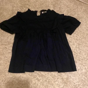 Svart blus med volang från Gina Tricot - Supersöt svart blus från Gina Tricot med volangdetaljer vid halsen och ärmarna.