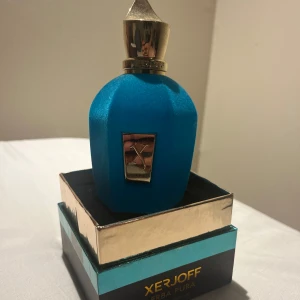 Xerjoff Erba Pura Eau de Parfum 100ml - Lyxig parfym från Xerjoff, Erba Pura, i en snygg blå flaska med gulddetaljer och exklusiv design. Flaskan rymmer 100 ml och har en elegant, matt yta med metallisk etikett och lock. Kommer i originalförpackning med guld- och turkosa detaljer.