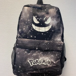Nattlysanse  Pokémon ryggsäck  - Cool svart ryggsäck med Gengar-ansikte och Pokémon-logga framtill. Väskan har ett galaxliknande mönster i vitt och grått, meshfickor på sidorna och justerbara axelband. Perfekt för dig som älskar Pokémon och vill sticka ut i skolan eller på stan. Helt ny , finns fler mönster kvar 