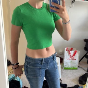 Grön croppad topp från Zara - Säljer en grön croppad topp från Zara med rund halsringning och korta ärmar. Toppen är ribbad och har en tight passform som sitter snyggt på kroppen, och är i ett lite tjockare material. Skriv om ni har frågor💕🥰