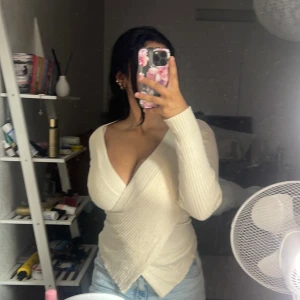 Ribbad omlottopp i ljus beige - Snygg ribbad omlottopp i ljus beige med djup v-ringning och långa ärmar. Toppen har en figurnära passform och omlott-design som ger en modern och trendig look. Perfekt att styla med jeans eller kjol för en chic vibe.