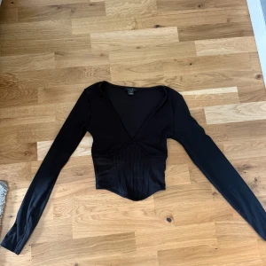 Svart långärmad  - Säljer en svart långärmad topp med djup v-ringning och markerad midja.