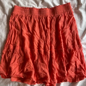 Korallfärgad volangkjol från Cubus - Säljer en korallfärgad kortkjol från Cubus i storlek M. Kjolen har en smockad midja och volangdetaljer. 