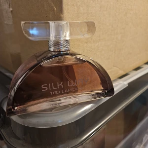 Silk Way parfym från Ted Lapidus - Silk Way från Ted Lapidus är en elegant parfym i en halvmåneformad flaska med transparent och bruntonat glas. Flaskan har ett stilrent, silvrigt halsband och ett brett, genomskinligt lock som ger en lyxig känsla. Perfekt för dig som gillar unika och snygga flaskor.