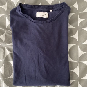Mörkblå t-shirt från Supply Project - Säljer En stilren mörkblå t-shirt från Supply Project i storlek S. T-shirten har klassisk rund halsringning och korta ärmar. Tillverkad i mjuk bomull som känns skön mot huden. Perfekt för en clean och enkel look. Tishan är i ett fint skick men lite skrynklig men då kan man använda ett strykjärn. Hojta till vid övriga funderingar 👍. 