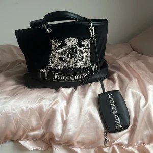Juicy Couture svart axelväska i sammet - Juicy Couture axelväska i svart sammet och skinn med silverfärgad logga och emblem framtill. Väskan har dubbla handtag, avtagbar liten väska och dragkedja. Insidan är fodrad med rosa tyg och svart logotypmönster. Perfekt för dig som gillar statement-accessoarer.köpt för 4000 aldrig använt 